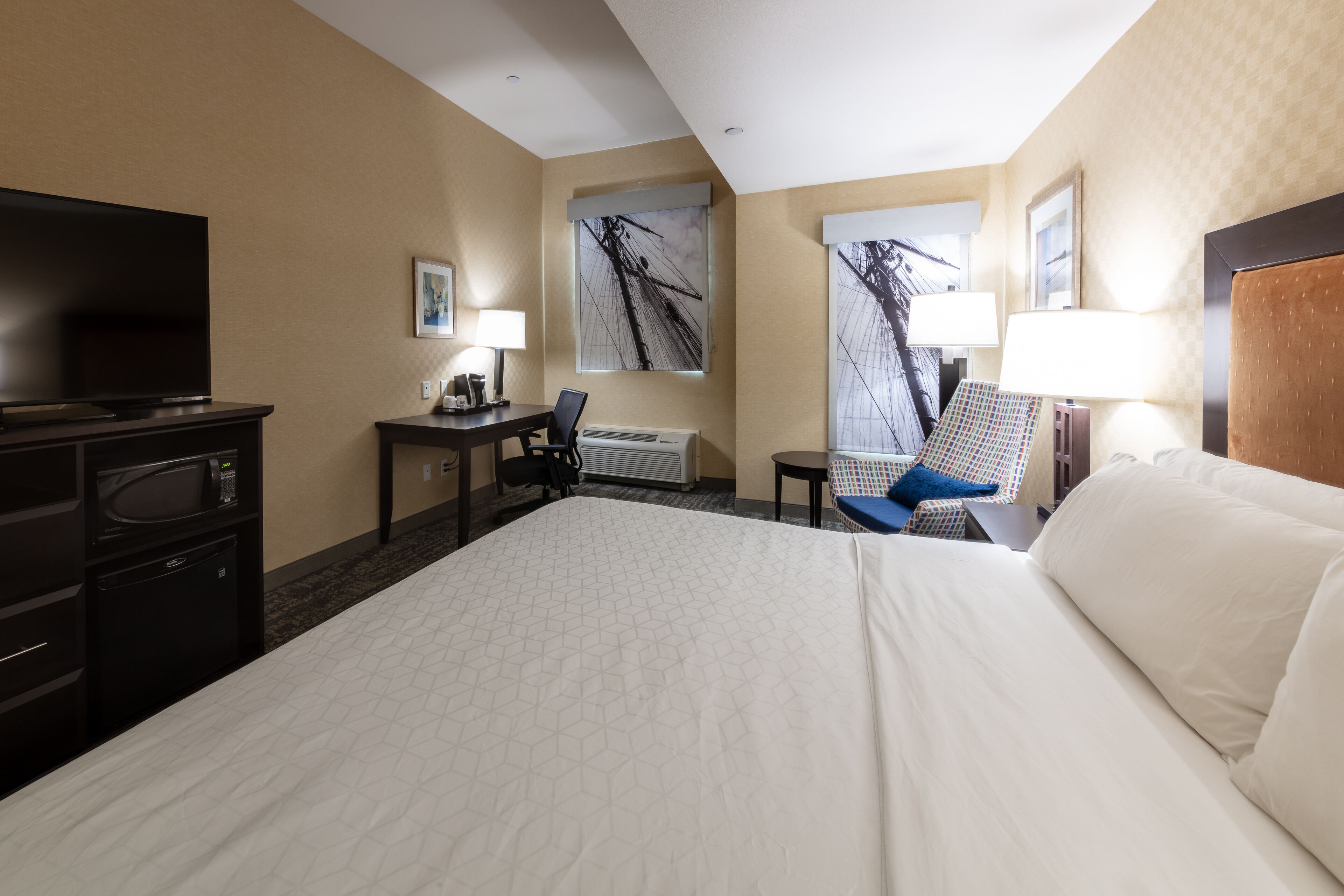 Una habitación de hotel con una cama grande, un escritorio con silla, televisor, lámpara y obras de arte en las paredes.