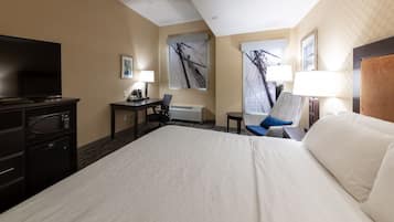 Una habitación de hotel con una cama grande, un escritorio con silla, televisor, lámpara y obras de arte en las paredes.