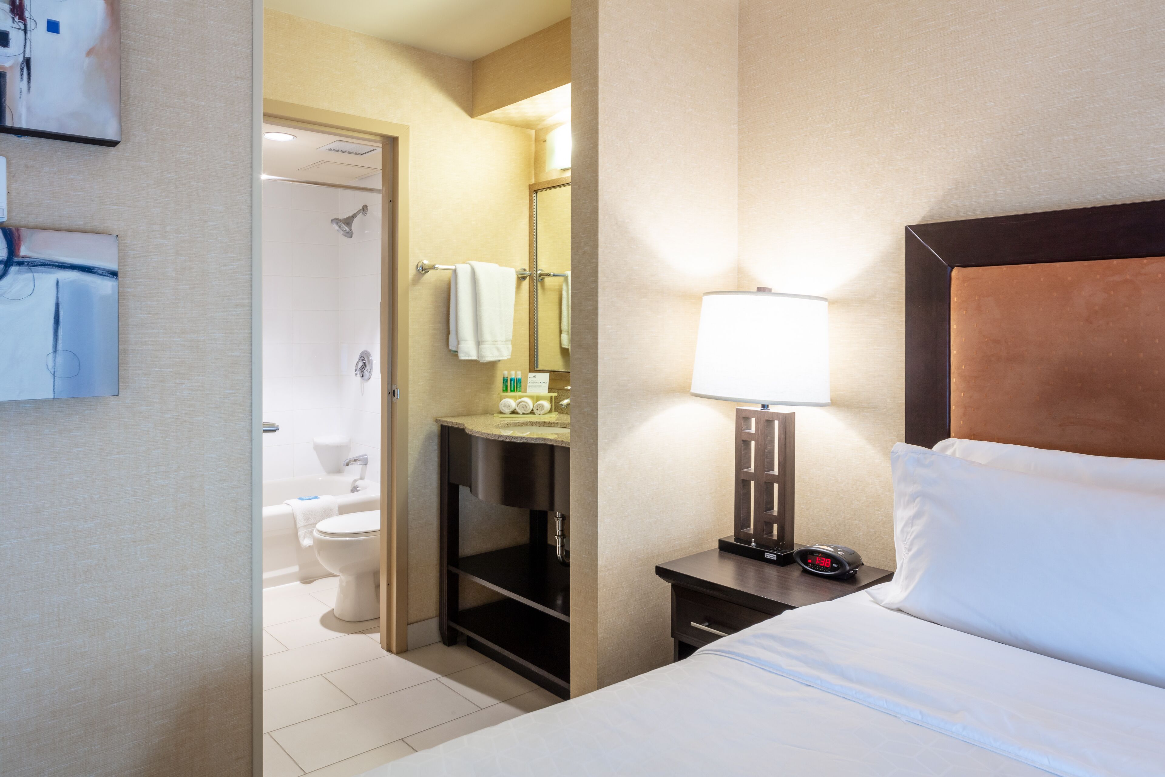A hotel room with a bed, a nightstand with a lamp, a bathroom with a toilet and a shower.