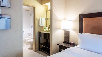 A hotel room with a bed, a nightstand with a lamp, a bathroom with a toilet and a shower.