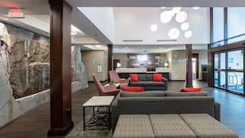 A spacious lobby with a stone wall, a grey sofa, a patterned ottoman, and a small table.