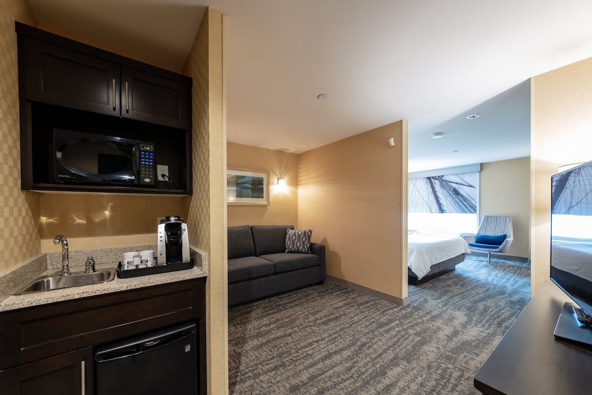 Une chambre d’hôtel équipée d’une kitchenette, d’un canapé, d’un lit, d’une télévision et d’une fenêtre donnant sur un paysage agréable.