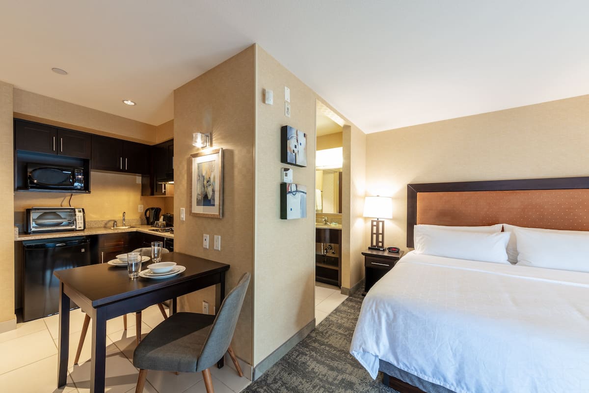 Ein Hotelzimmer mit Bett, Schreibtisch mit Stuhl, einer Mikrowelle, einem Kühlschrank und einem sichtbaren Badezimmer durch eine offene Tür.