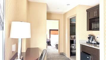 Quarto de hotel com mesa de jantar, luminária, micro-ondas, máquina de café e geladeira.