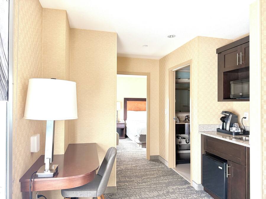 Quarto de hotel com mesa de jantar, luminária, micro-ondas, máquina de café e geladeira.