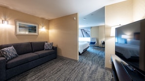 A hotel room with a dark gray sofa, a flat-screen TV, a bed, and a large window. - Holiday Inn Express Hotel & Suites Riverport Richmond by IHG (Richmond)