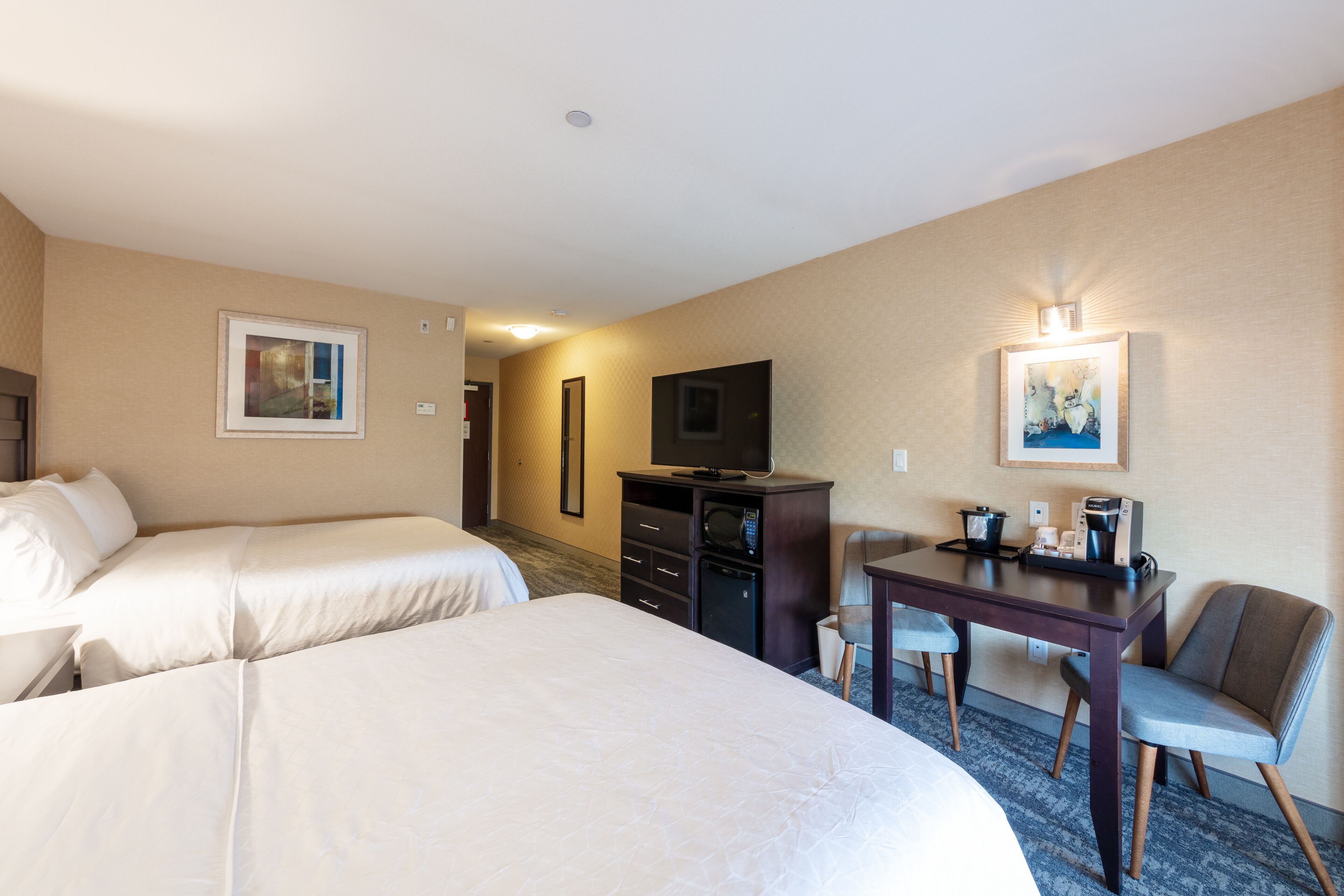 A hotel room with two beds, a desk with a chair, a television, and a microwave.