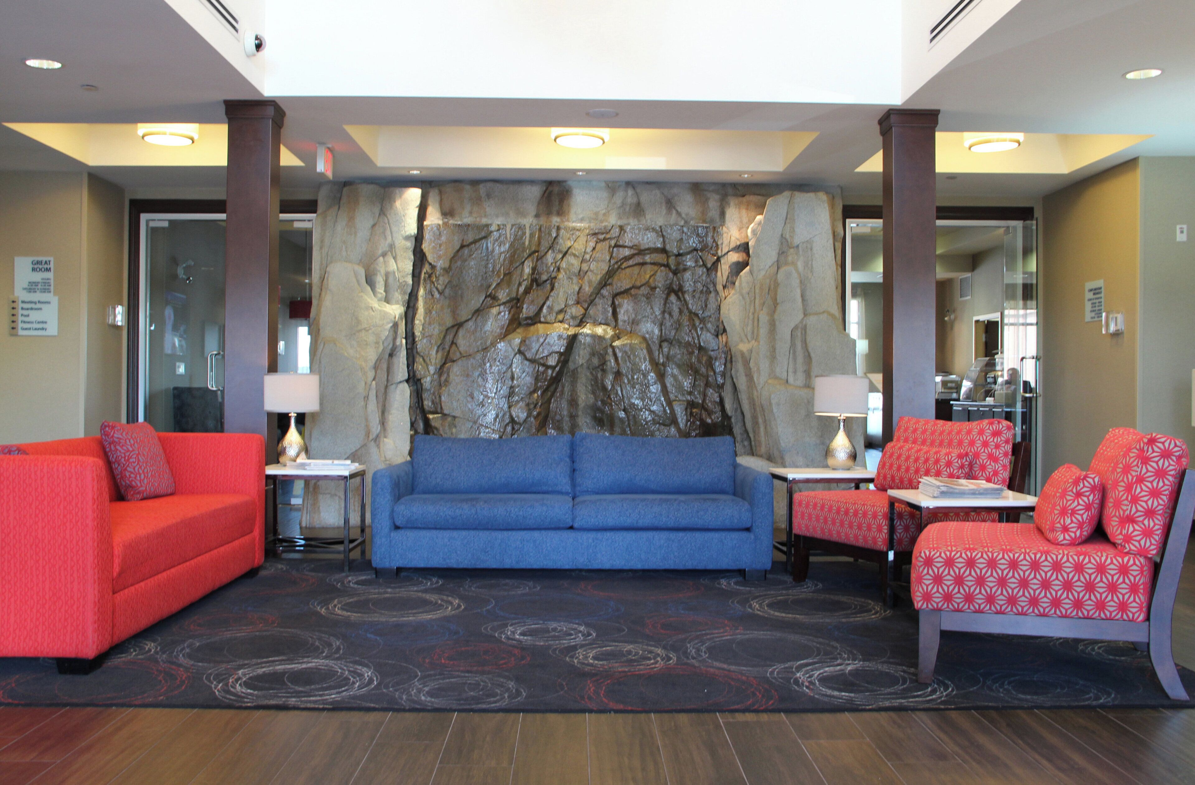 A lobby with a blue sofa, red armchairs, a stone wall, and a small table with a lamp.
