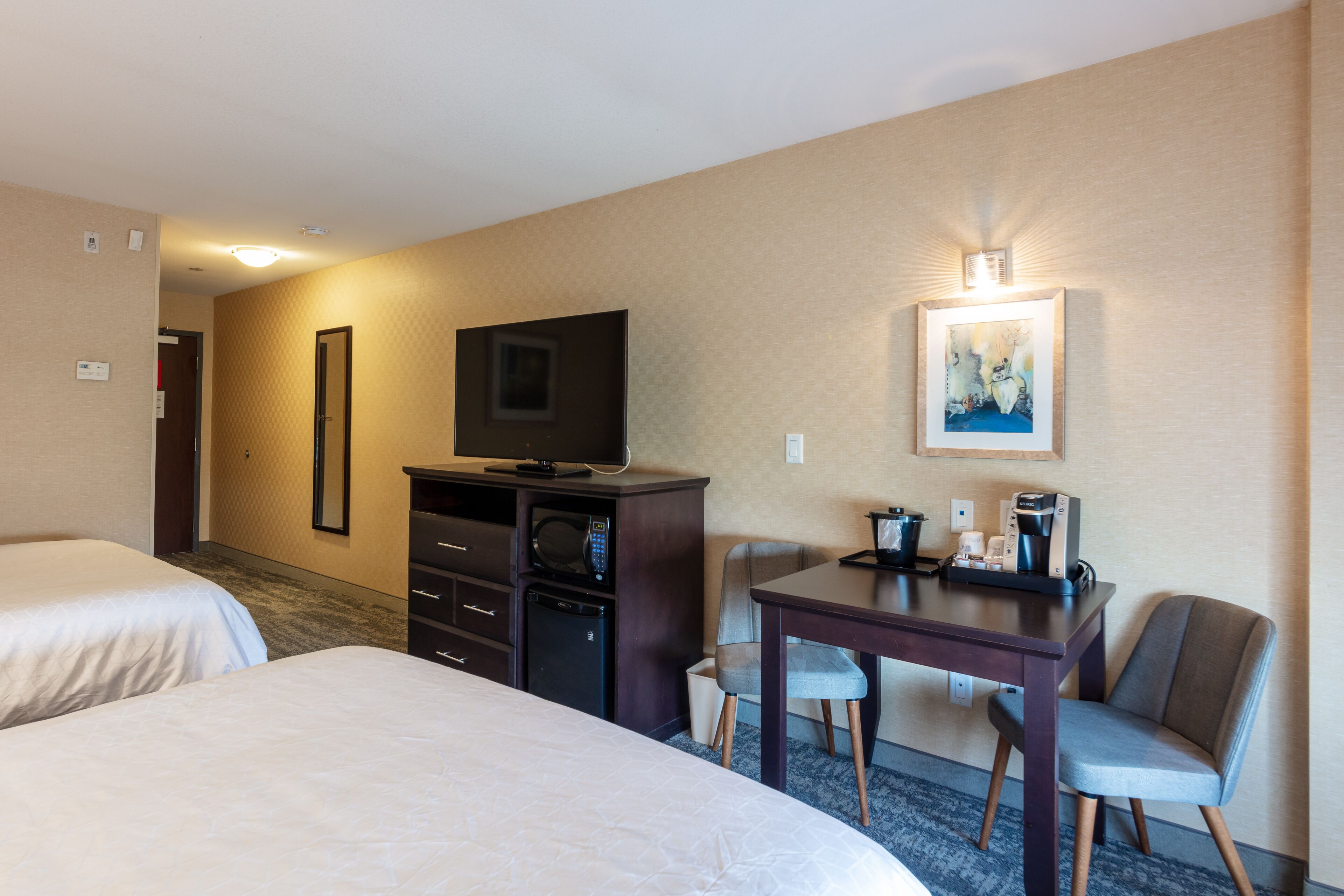Habitación de hotel con dos camas, un escritorio con sillas, televisor, microondas y cafetera.