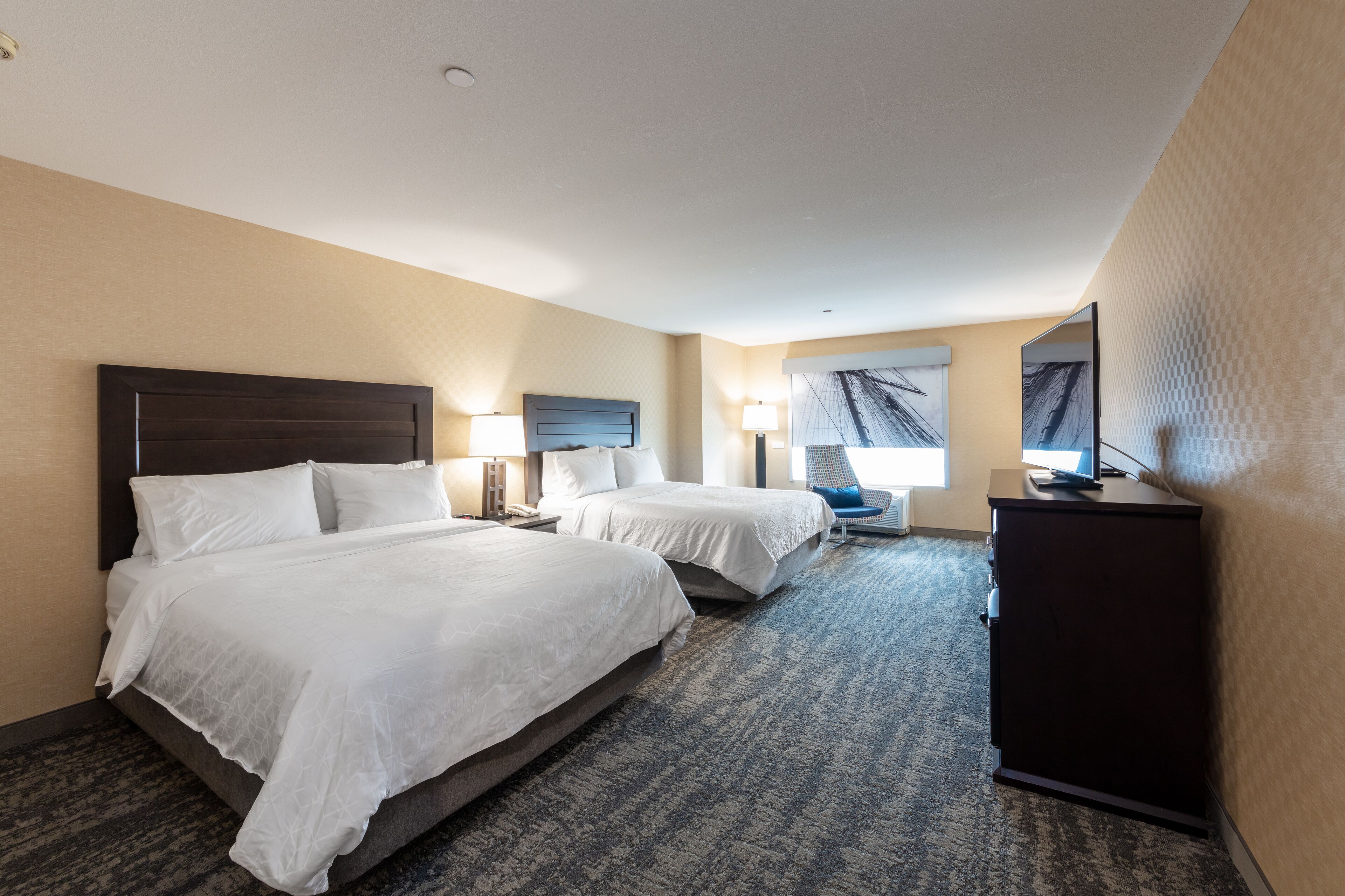 A hotel room with two beds, a desk, a chair, and a television.