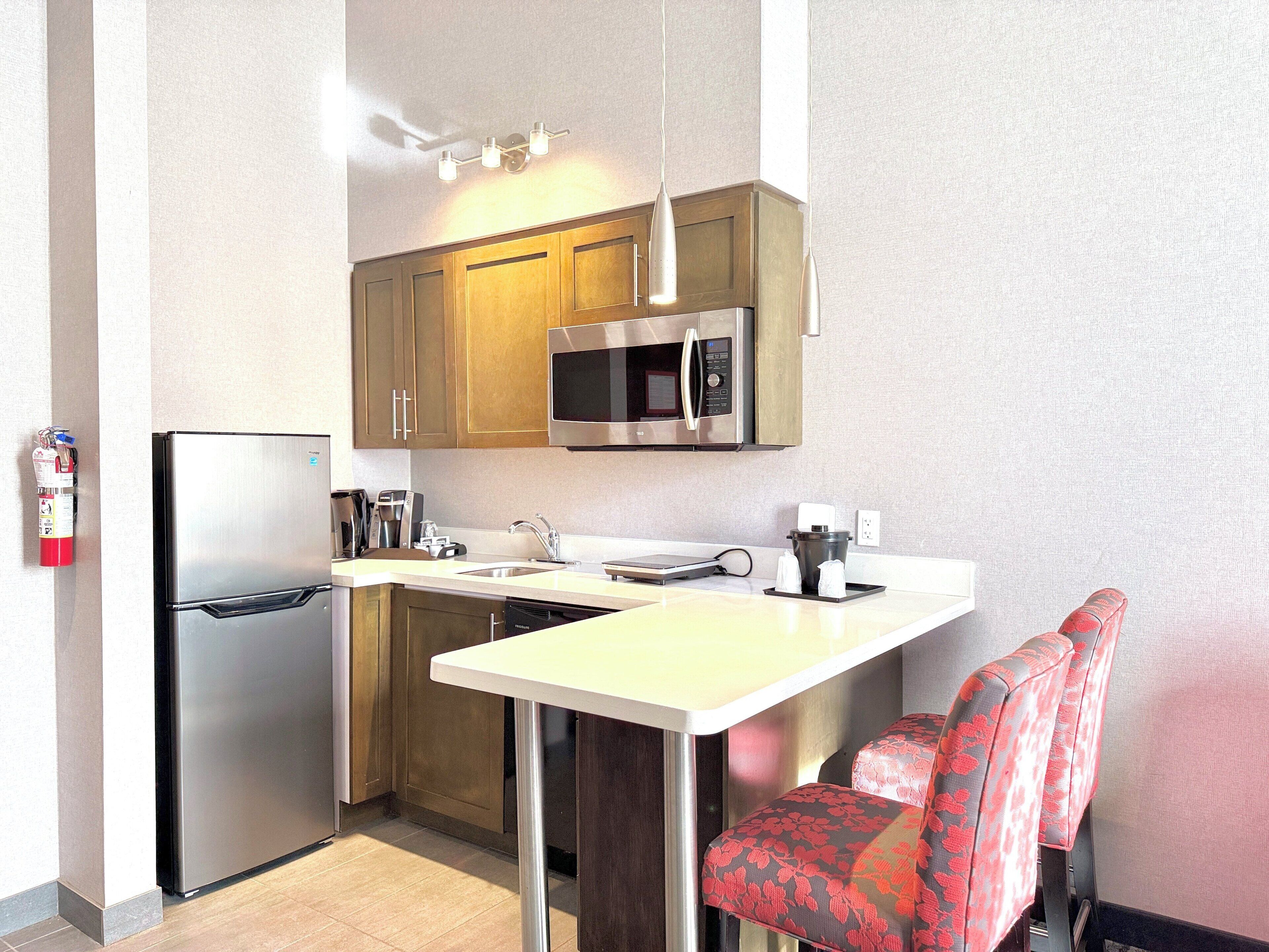 A compact kitchen with a refrigerator, microwave, sink, and a small dining area with chairs.
