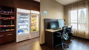 A hotel room with a desk, two chairs, a refrigerator stocked with beverages, and a 'No Food or Drink' sign.