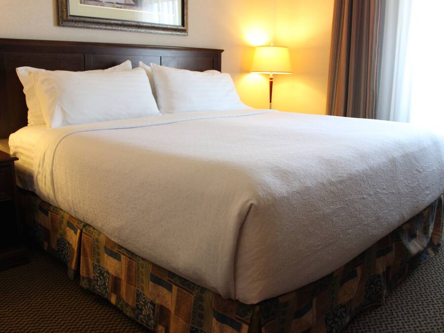 Una cama bien hecha con cabecera de madera, una lámpara de noche y falda de cama estampada.