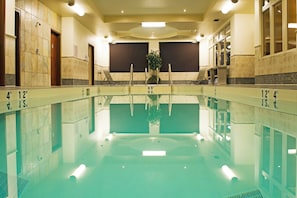 A large indoor swimming pool with clear water, marked depth lines, and a central plant.