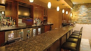 A bar area with a granite countertop, multiple liquor bottles, glasses, and a television. - Holiday Inn Hotel & Suites West Edmonton by IHG (Edmonton)