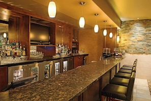 A bar area with a granite countertop, multiple liquor bottles, glasses, and a television.