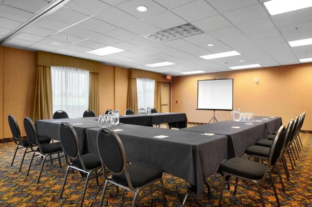Une salle de conférence avec une longue table, des chaises, un écran de projection et un sol recouvert de moquette.