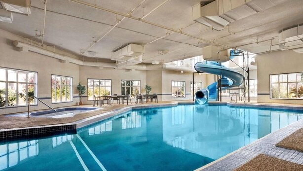 An indoor swimming pool with a blue slide, large windows, and a high ceiling with visible ductwork. - Days Inn & Suites by Wyndham Strathmore (Strathmore)