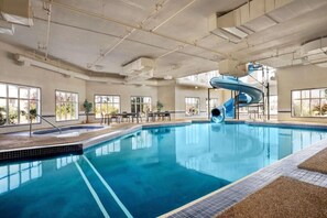 An indoor swimming pool with a blue slide, large windows, and a high ceiling with visible ductwork. - Days Inn & Suites by Wyndham Strathmore (Strathmore)