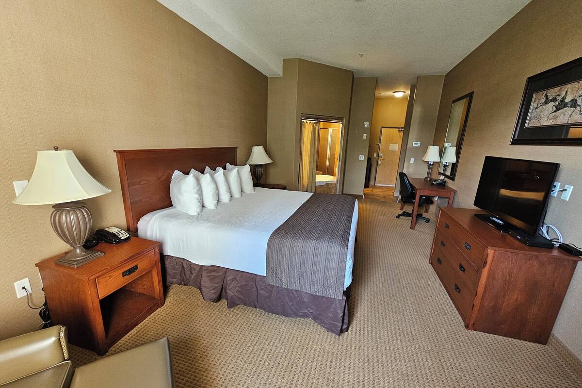 Une chambre d’hôtel avec un grand lit, un bureau avec une télévision, une chaise et une lampe.