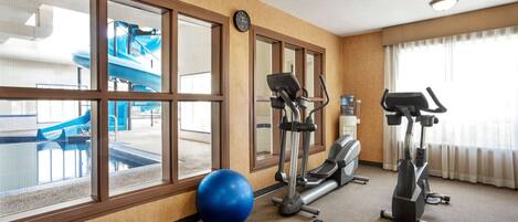 Un gimnasio con equipo de ejercicios, una pelota de ejercicio azul y vistas a un tobogán acuático interior.