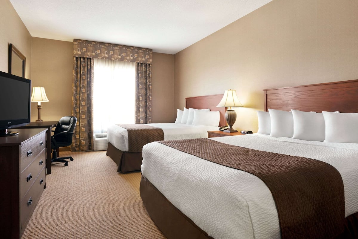 Une chambre d’hôtel avec deux lits, un bureau avec une télévision, une chaise et une lampe.