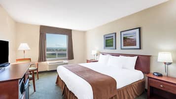 Ein Hotelzimmer mit einem großen Bett, einem Schreibtisch, einem Sessel, einem Fernseher, zwei gerahmten Bildern an der Wand und einem Fenster mit Blick ins Freie.