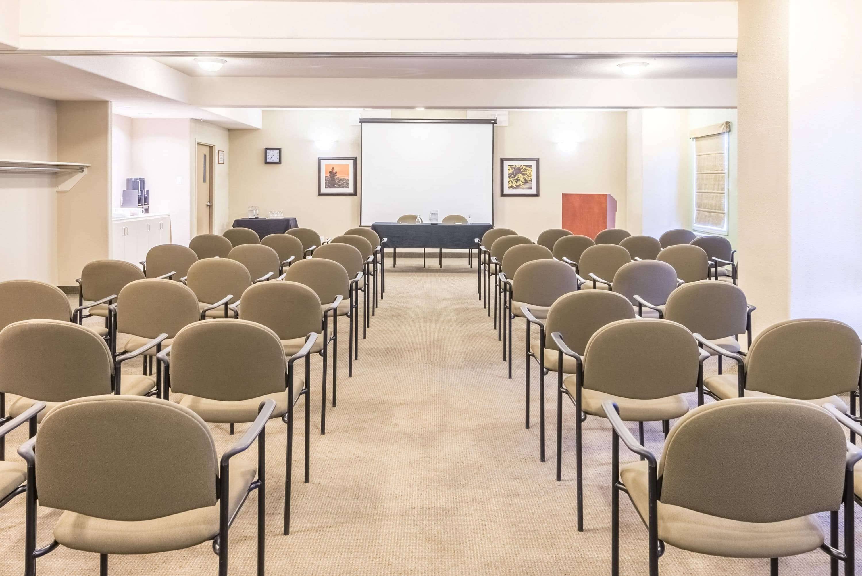 Une salle de conférence avec des rangées de chaises disposées face à un tableau blanc et à un écran de projection.