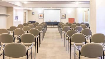 Uma sala de conferências com fileiras de cadeiras voltadas para um quadro branco e uma tela de projetor.
