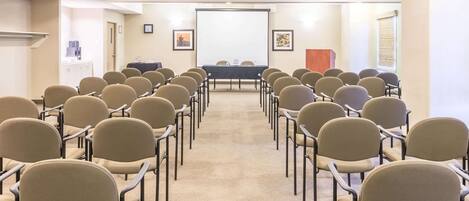 Un salón de conferencias con filas de sillas orientadas hacia una pizarra y una pantalla de proyector.