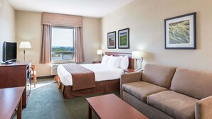 Una habitación de hotel con cama, sofá, escritorio, televisor y ventana con cortinas.