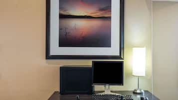 Een bureau met een computer, een lijst met een foto van een ondergaande zon boven water, en een lamp.