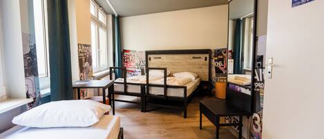 A hotel room with a bed, a desk, a chair, a mirror, and a window.