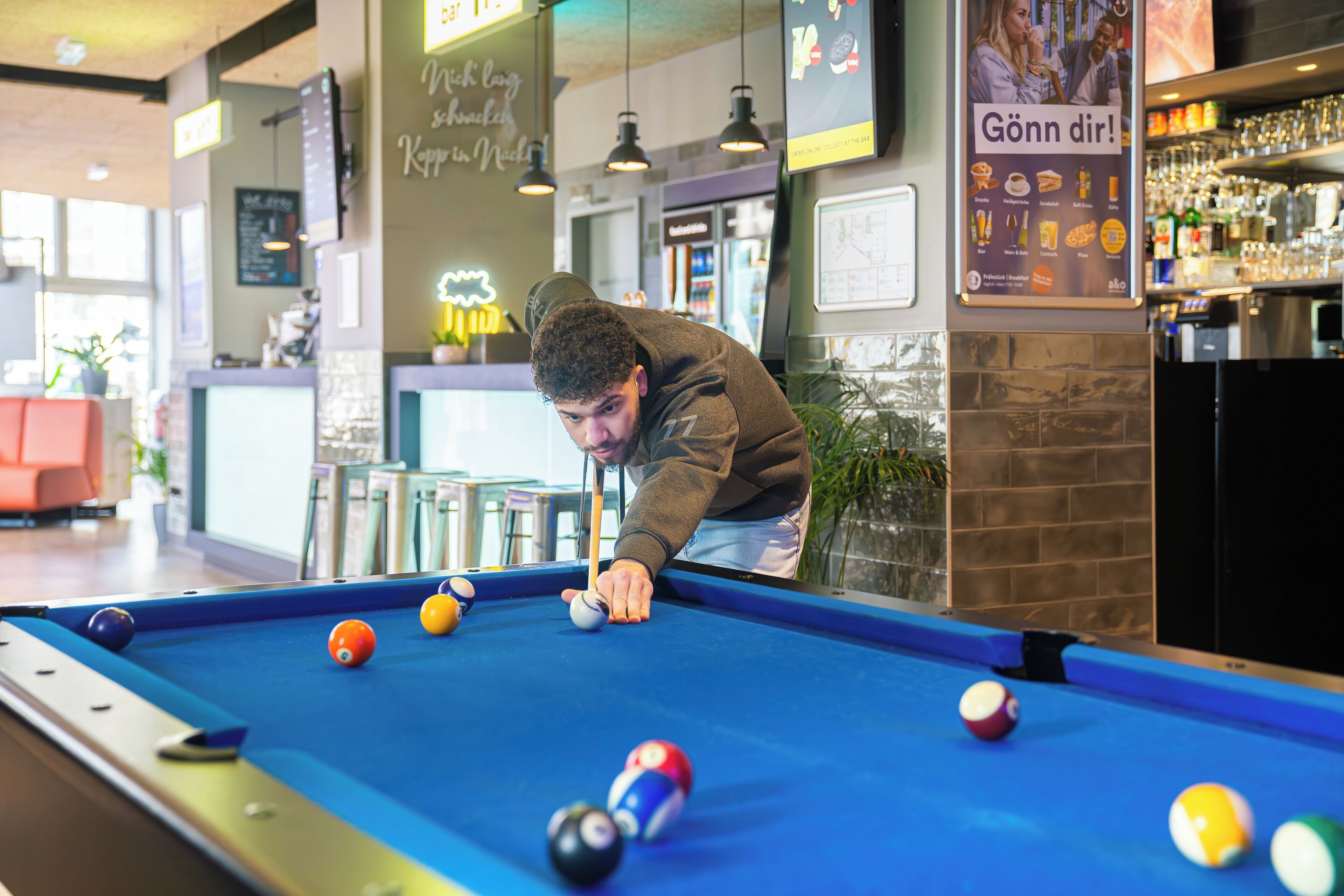 A pool table with balls, a bar area with glasses and bottles, and a seating area with chairs.