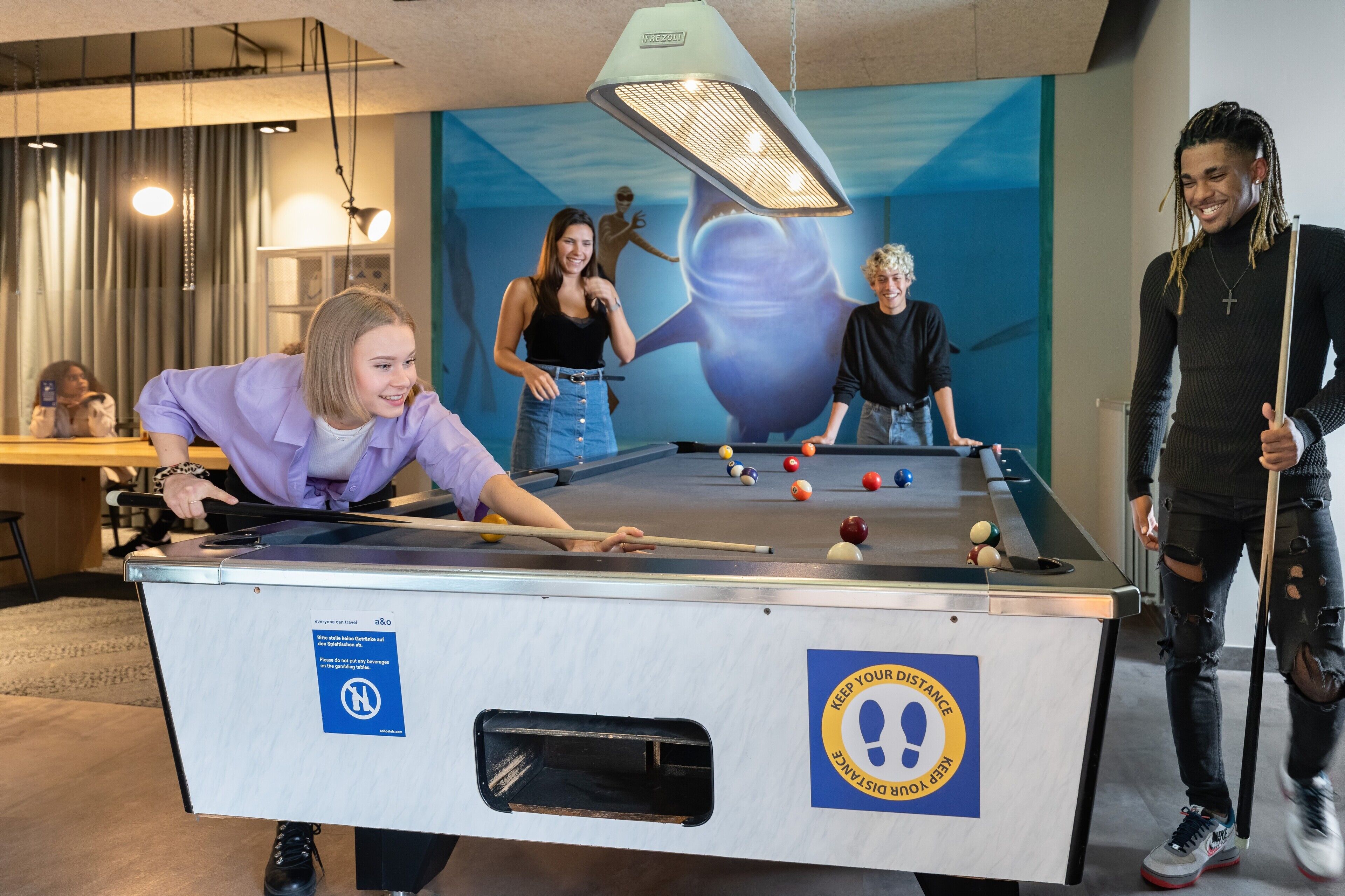 A pool table in a room with a mural on the wall, a ceiling light, and a sign on the table.