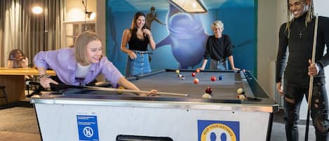 A pool table in a room with a mural on the wall, a ceiling light, and a sign on the table.