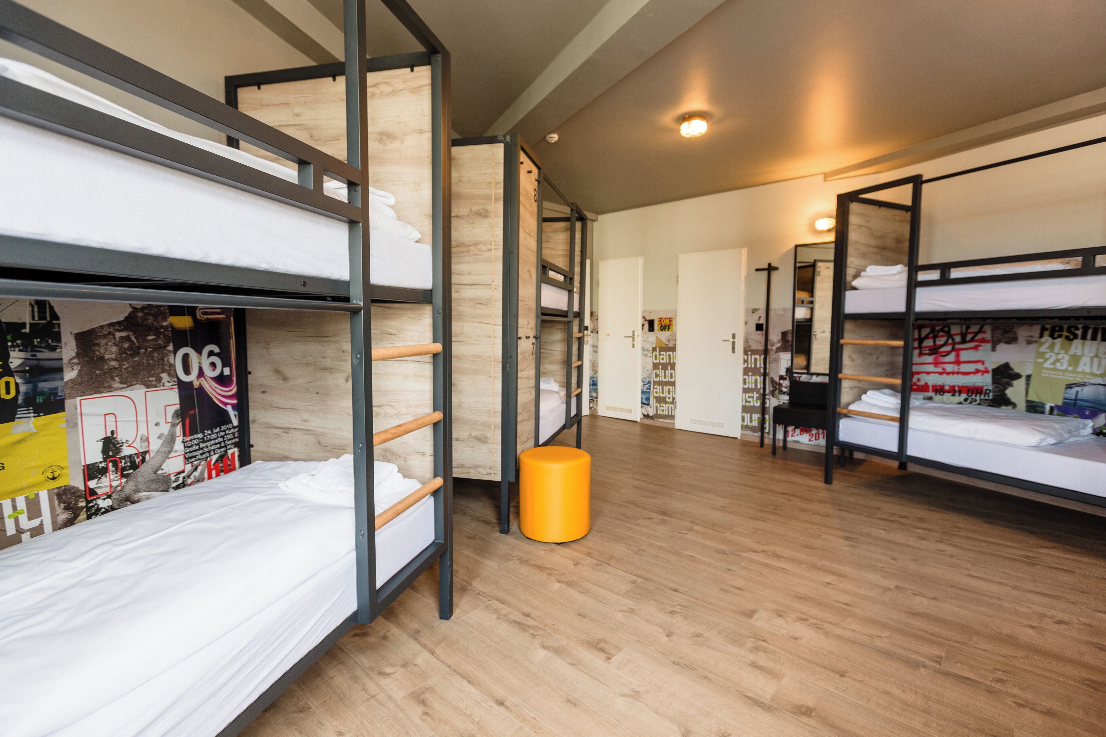 A dormitory room with bunk beds, a wooden floor, and a poster on the wall.