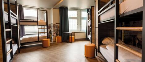 A dormitory room with bunk beds, a small table, and a window with curtains.