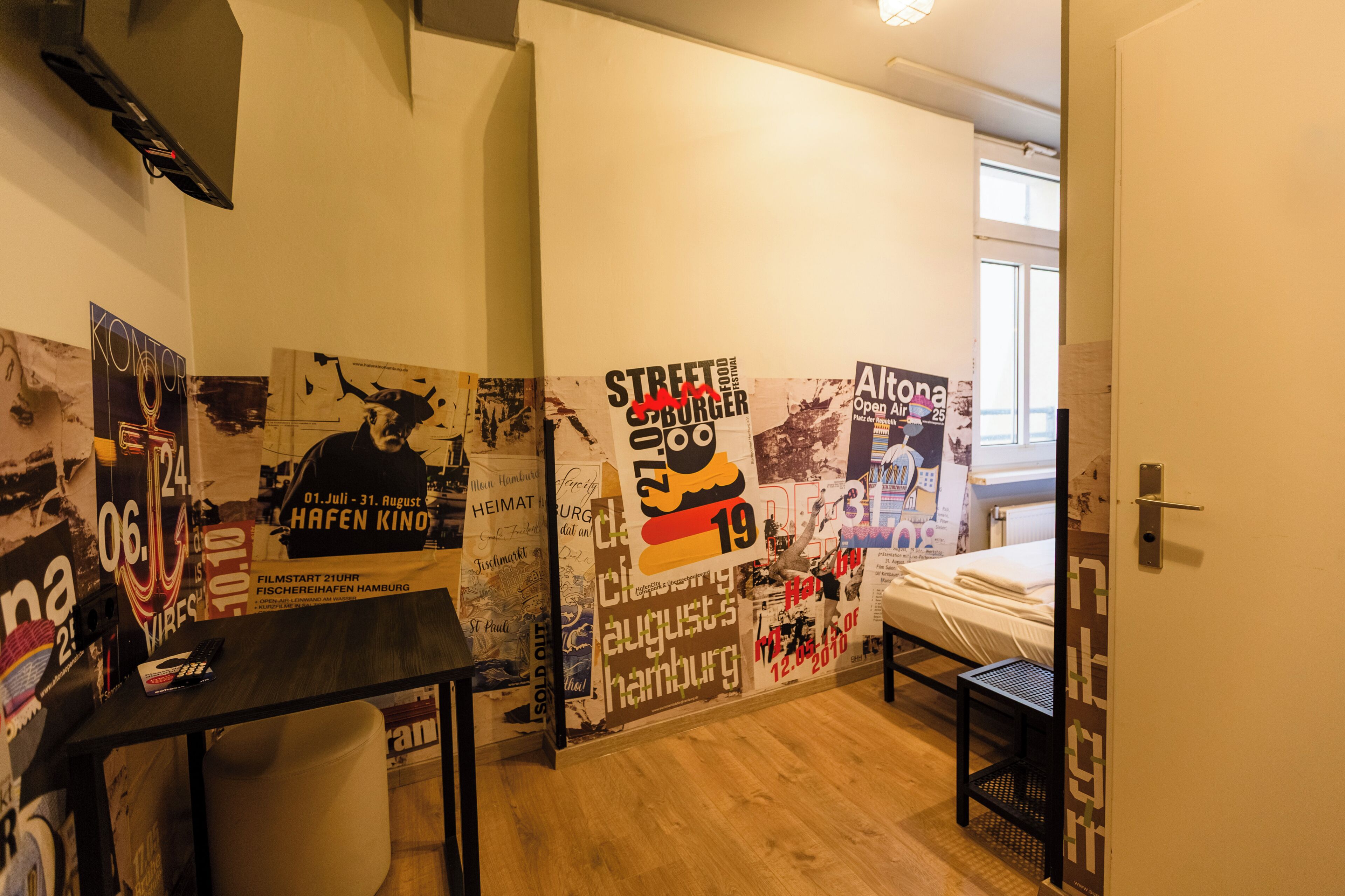A room with a bed, a desk, and a wall covered with various posters and flyers.