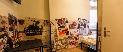 A room with a bed, a desk, and a wall covered with various posters and flyers.