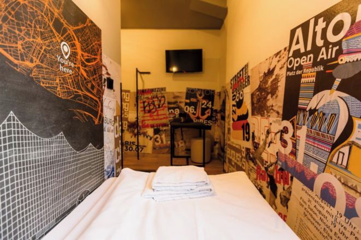 Une chambre d’hôtel avec un lit, des affiches aux murs, un téléviseur à écran plat et une petite table.