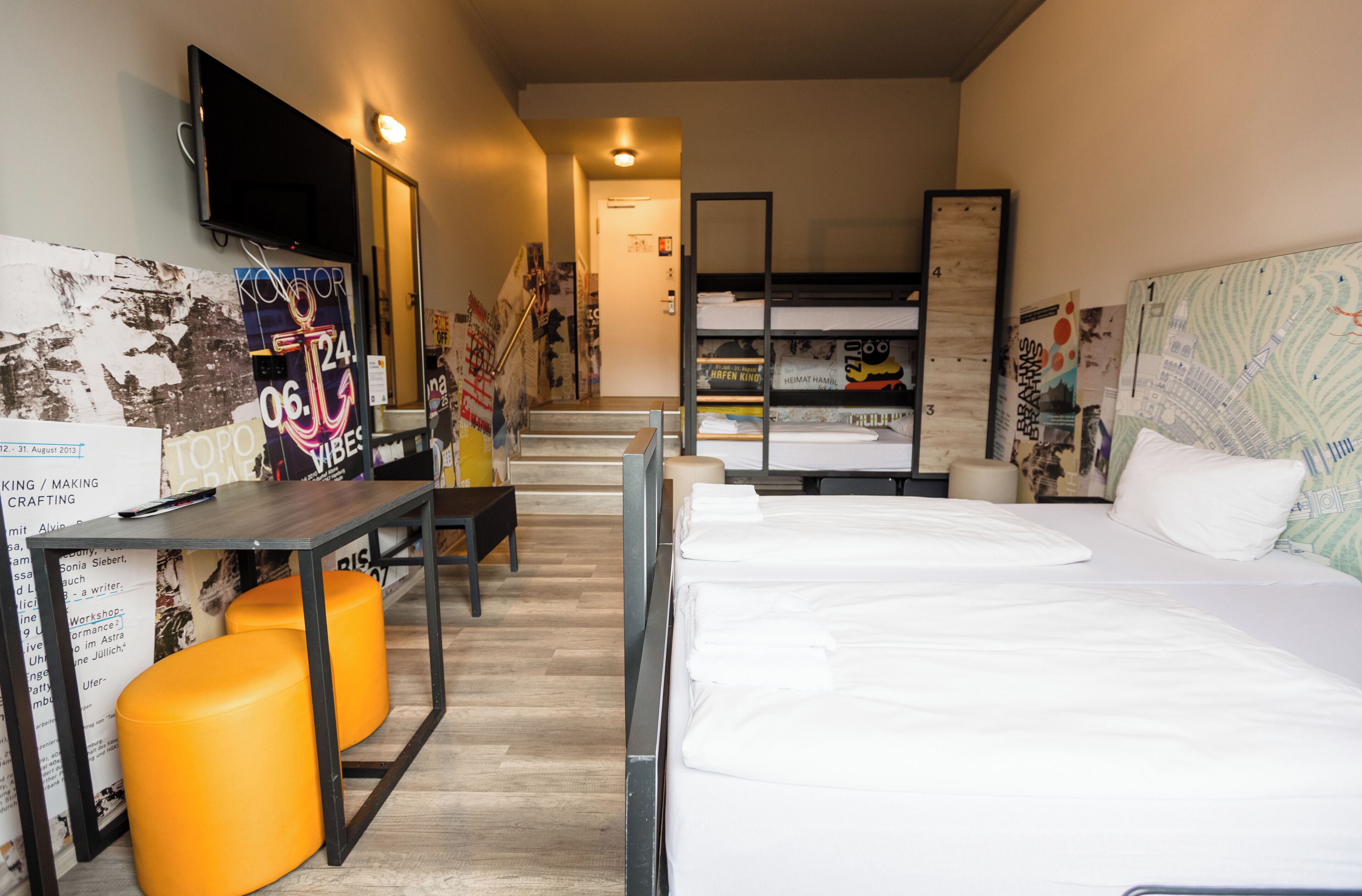 Habitación de hotel con literas, un escritorio con silla, un televisor montado en la pared y un cartel en la pared.