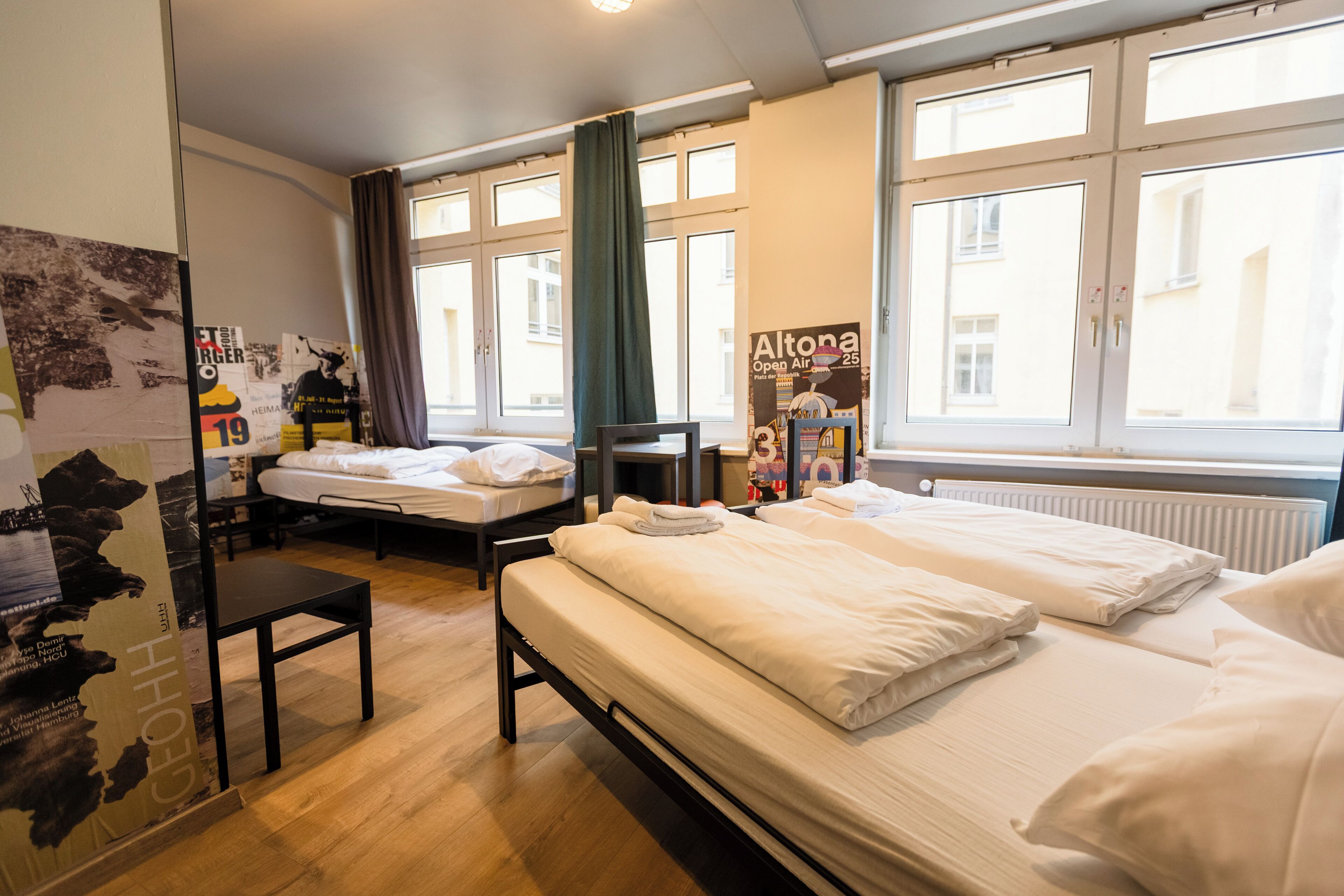 Et hotelværelse med to senge, et skrivebord, en stol og store vinduer.