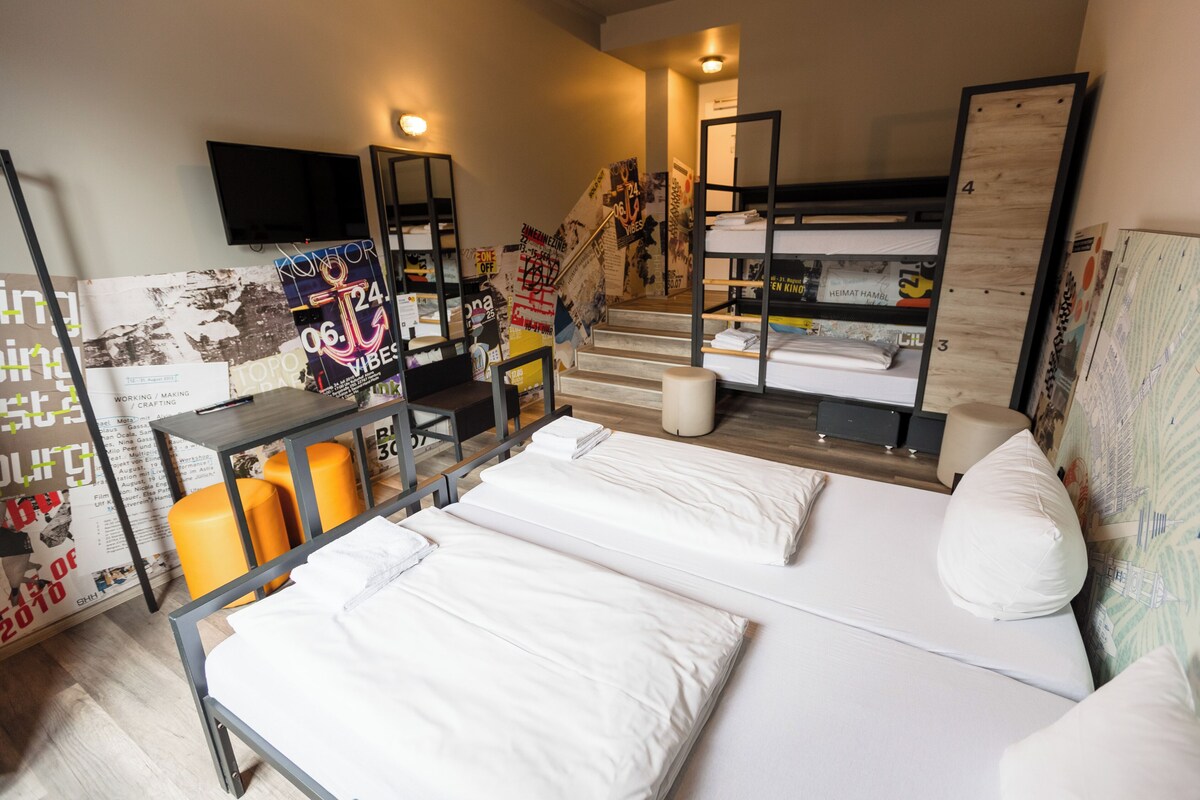Een kamer met stapelbedden, een bureau met stoel, een aan de muur bevestigde televisie en een trap.