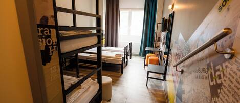 A room with bunk beds, a desk, a chair, and a window with curtains.