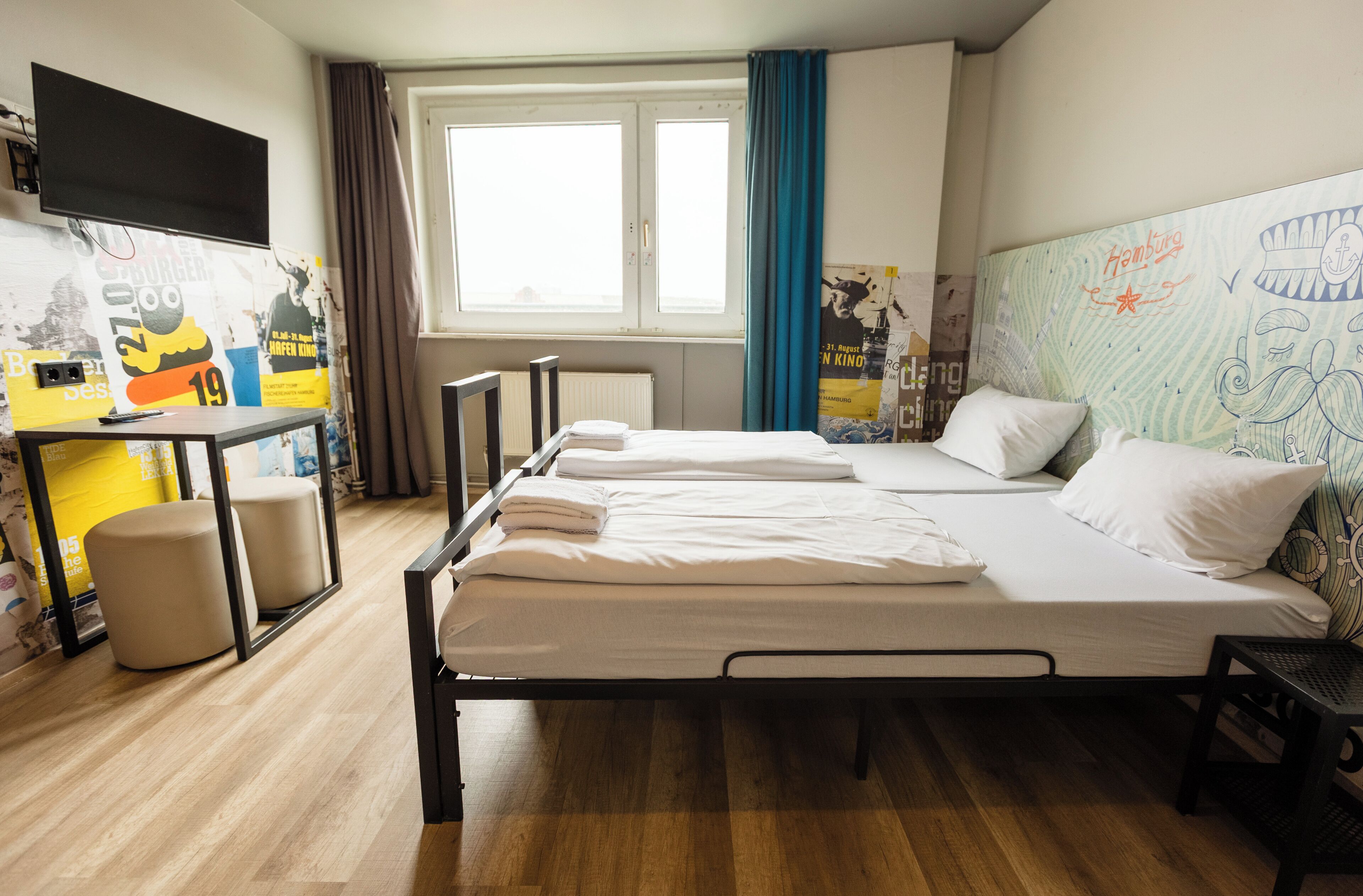 Habitación de hotel con cama, escritorio, silla, ventana con cortinas y una pared con un mapa y texto.
