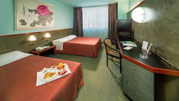 Ein Hotelzimmer mit zwei Betten, einem Schreibtisch mit Stuhl, einem Fernseher und einem Bild an der Wand.