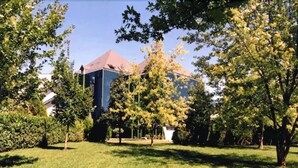 Un bâtiment à l’architecture moderne, entouré d’un espace verdoyant bien entretenu, agrémenté d’arbres.
