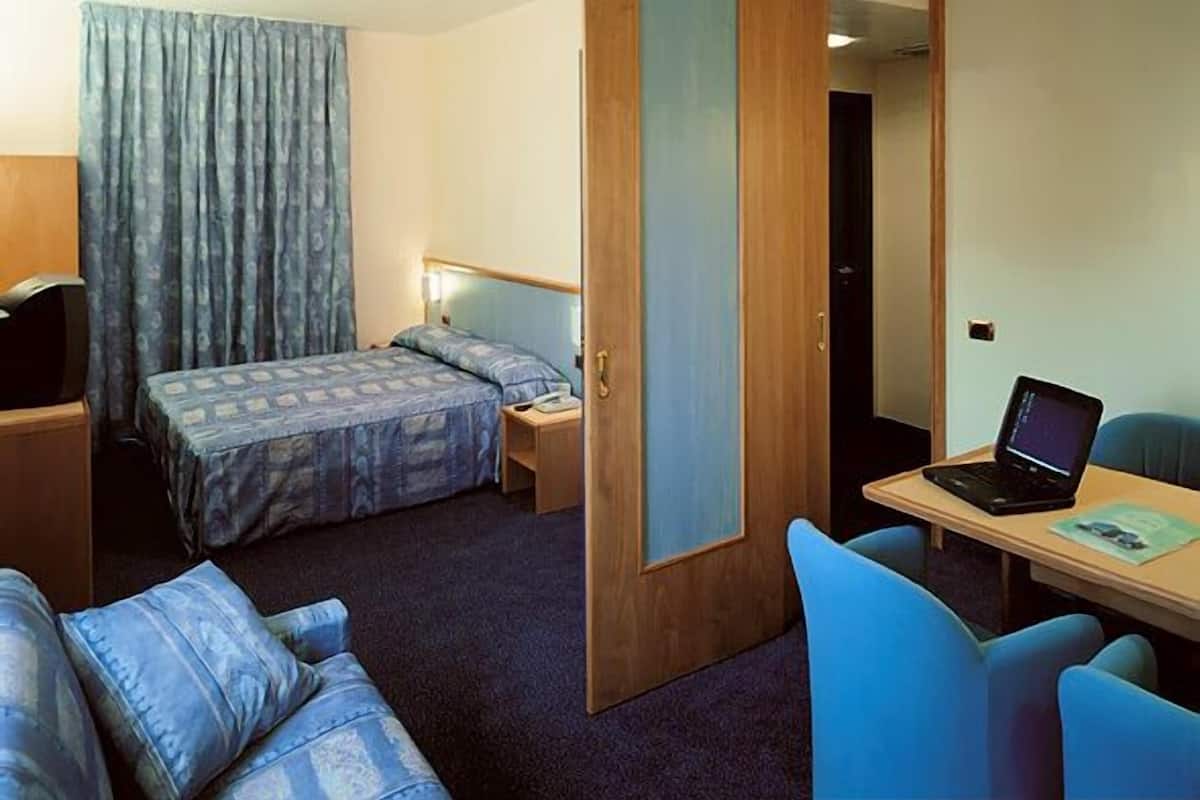 Ein Hotelzimmer mit einem Bett, einem Schreibtisch mit Laptop, einem Sessel und einer Couch.
