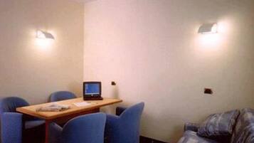 Uma pequena sala de reuniões com uma mesa de madeira, quatro cadeiras azuis, um laptop e duas luzes fixadas na parede.
